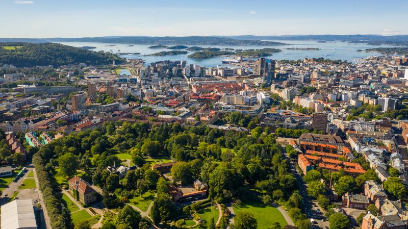 F�gelvy �ver centrala Oslo p� sommaren, med en gr�nskande park i f�rgrunden och Oslofjorden som brder ut sig i fj�rran; d�remellan stadsbebyggelse.